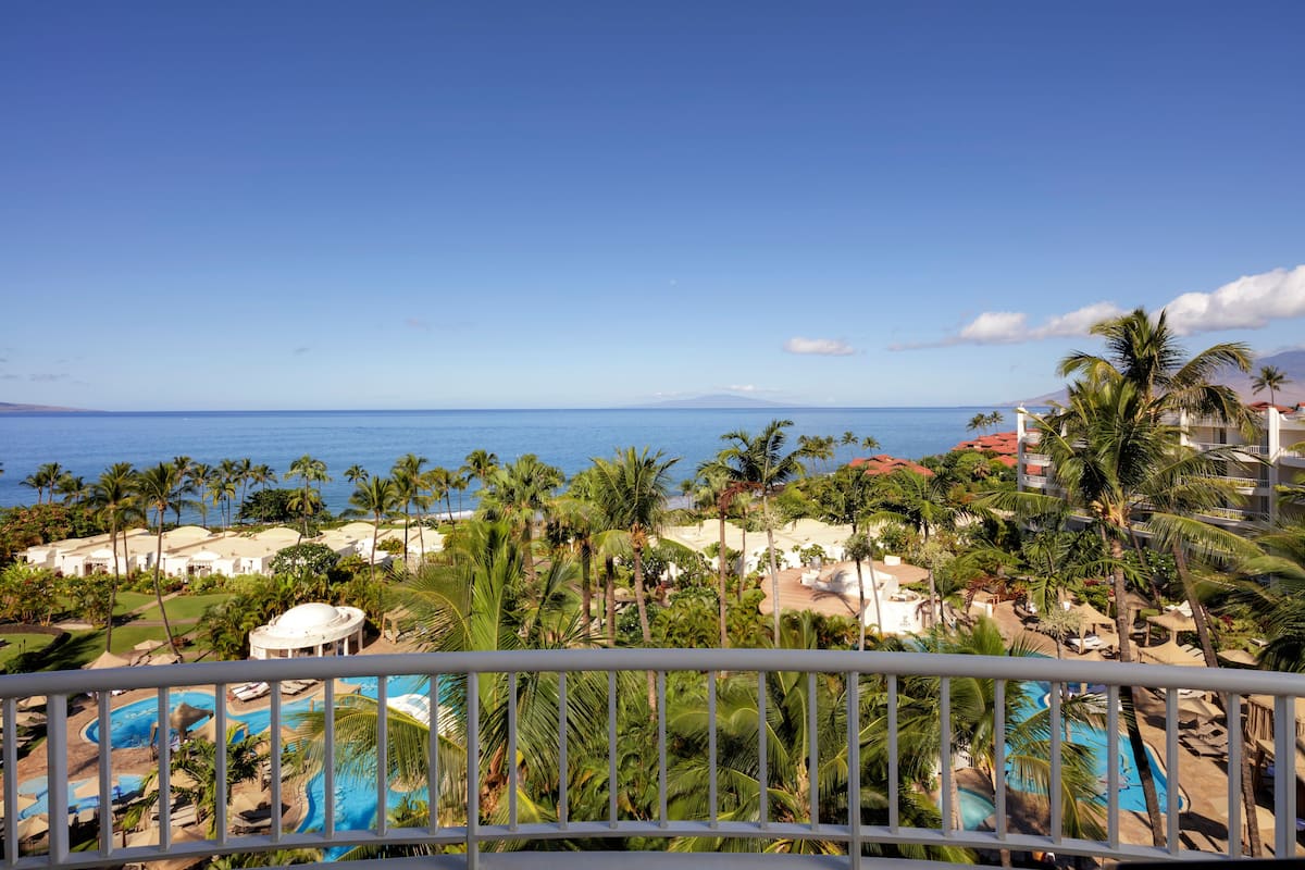 A resort with a pool area, palm trees, and a view of the ocean.