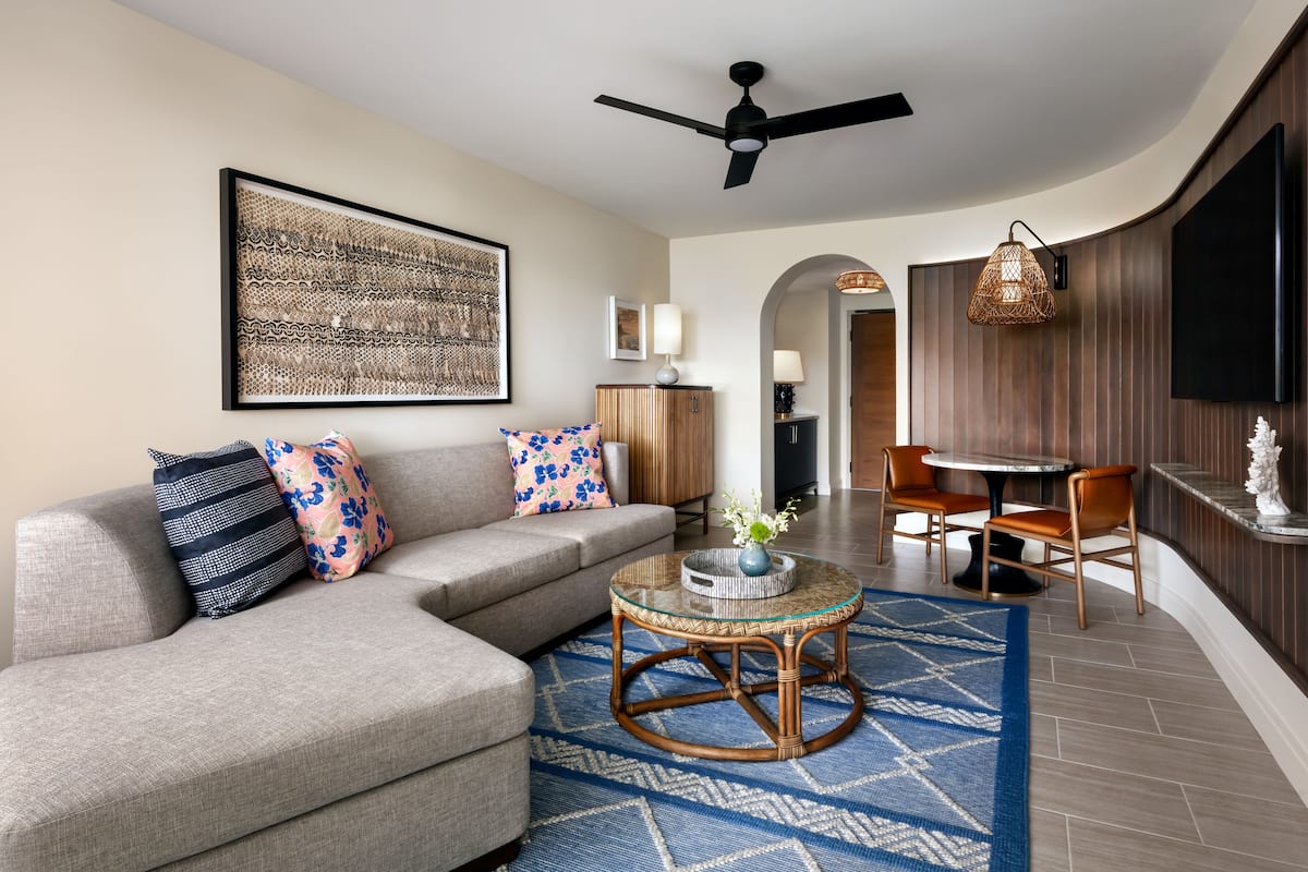 A modern living room with a grey sofa, patterned cushions, a glass coffee table, and a blue patterned rug.