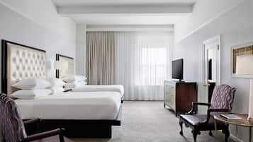 Habitación de hotel con una cama grande, dos sillas, un escritorio, un televisor y una ventana con cortinas.