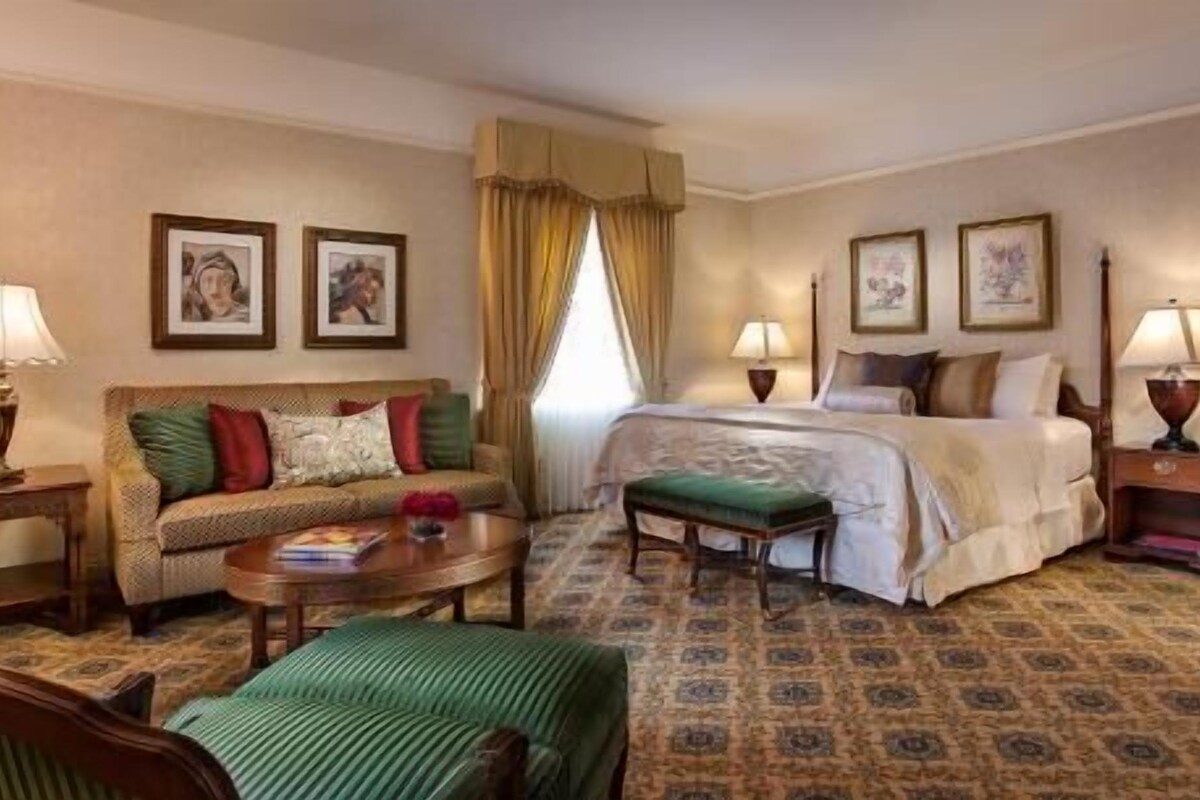 A hotel room with a bed, a sofa, a small table, a chair, and two lamps.
