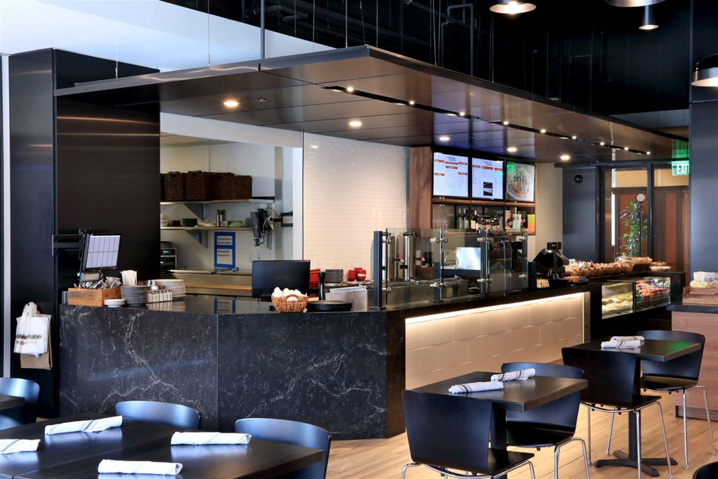 A modern restaurant with a marble counter, black chairs, and a visible kitchen area.