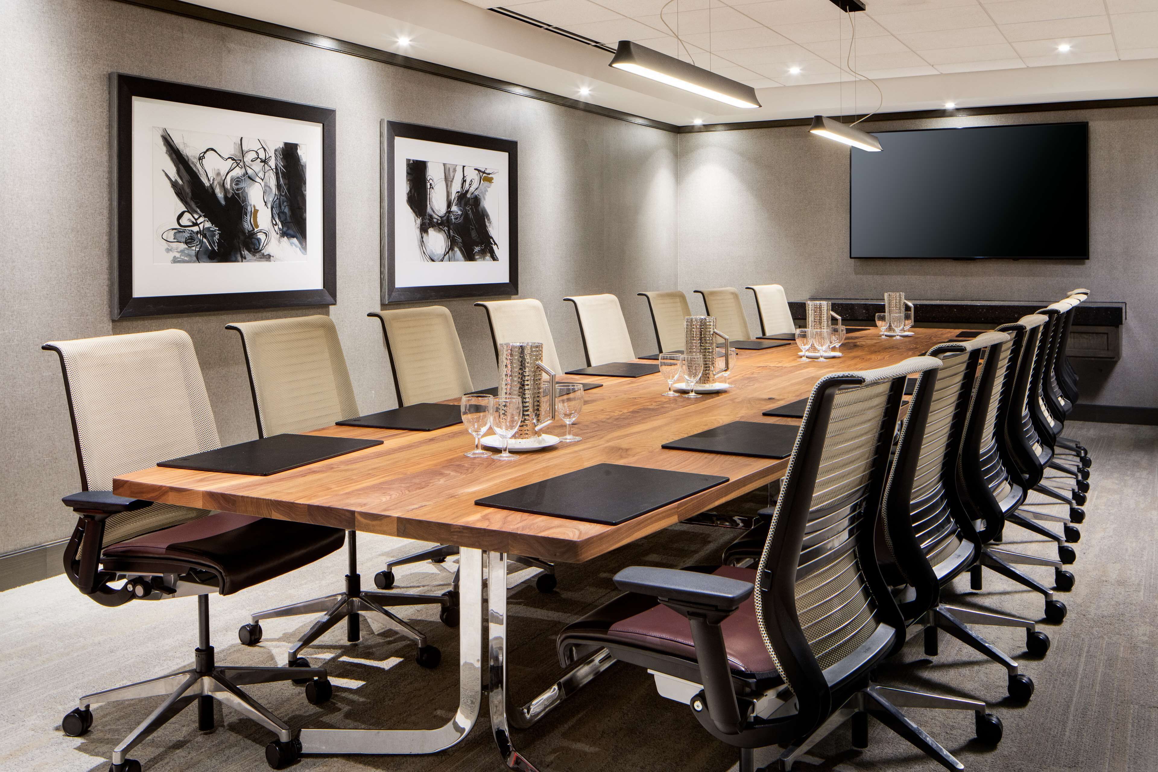 A conference room with a long table, chairs, and a large screen.