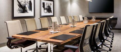 A conference room with a long table, chairs, and a large screen.