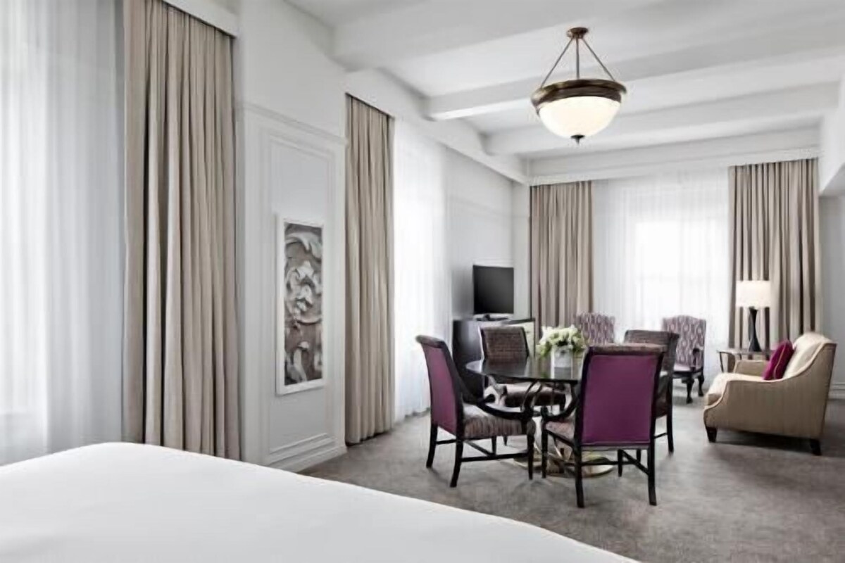 A hotel room with a bed, a dining table with chairs, a TV, and a sofa.