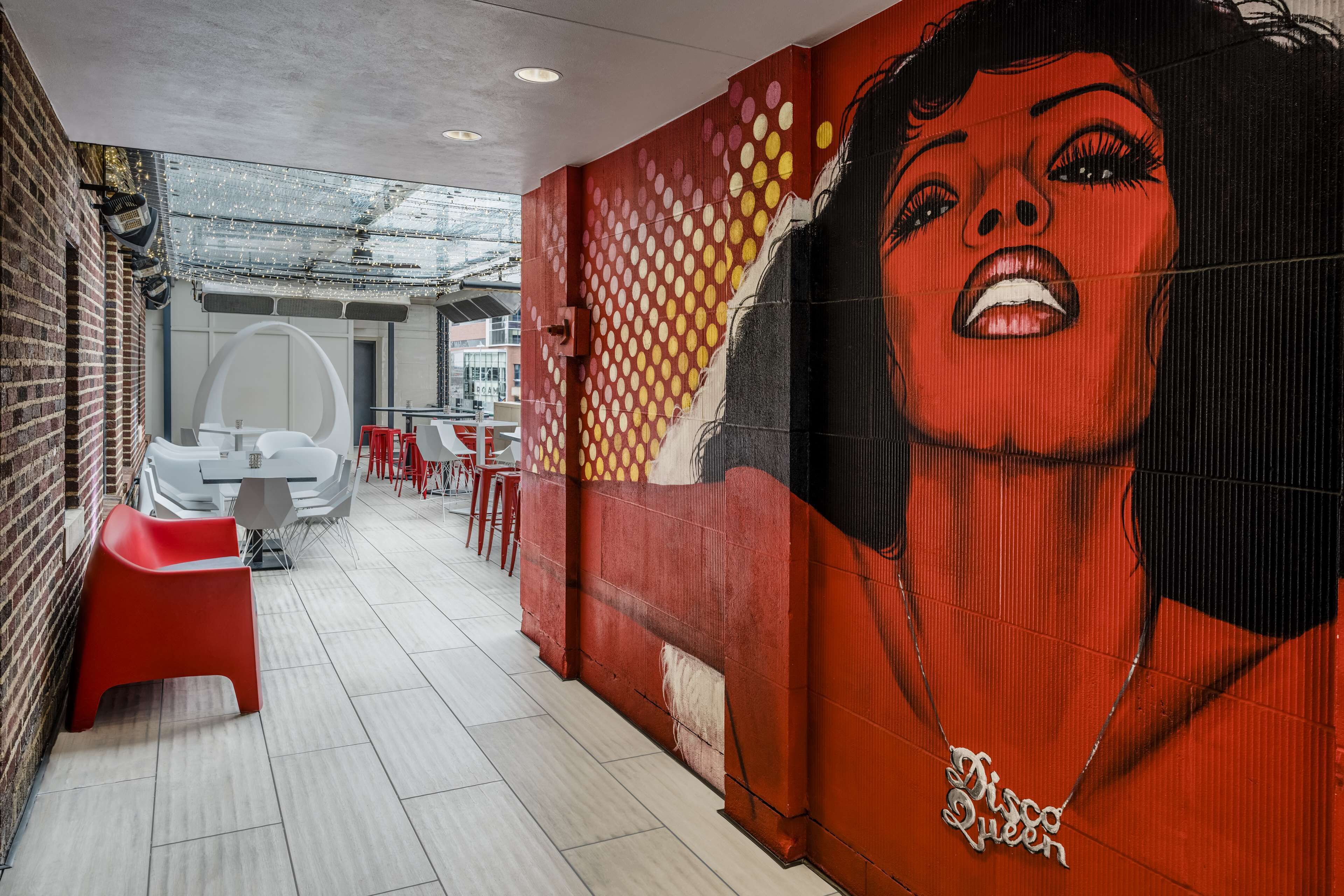 A corridor with a mural, red chairs, and tables.
