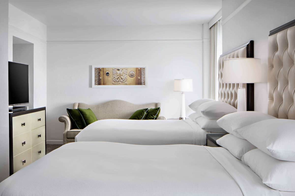 Ein Hotelzimmer mit zwei Betten, einem Fernseher, einer Lampe und einer Wanddekoration.
