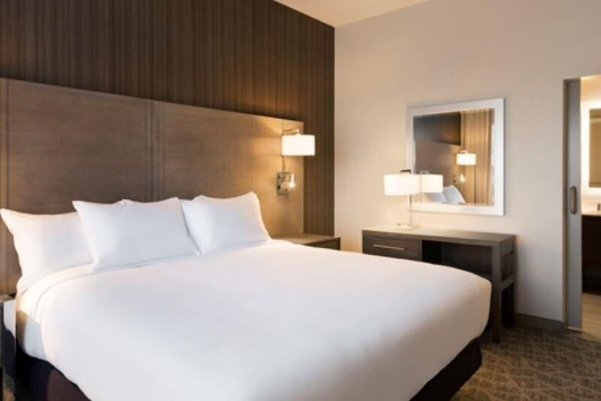 A hotel room with a large bed, bedside lamps, a mirror, and a wooden headboard.