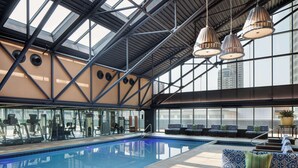 An indoor swimming pool with exercise equipment, seating areas, and a high ceiling with skylights. - Amway Grand Plaza, Curio Collection by Hilton (Grand Rapids)