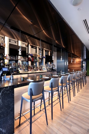 A modern bar area with a long counter, bar stools, and a variety of bottles and glasses.