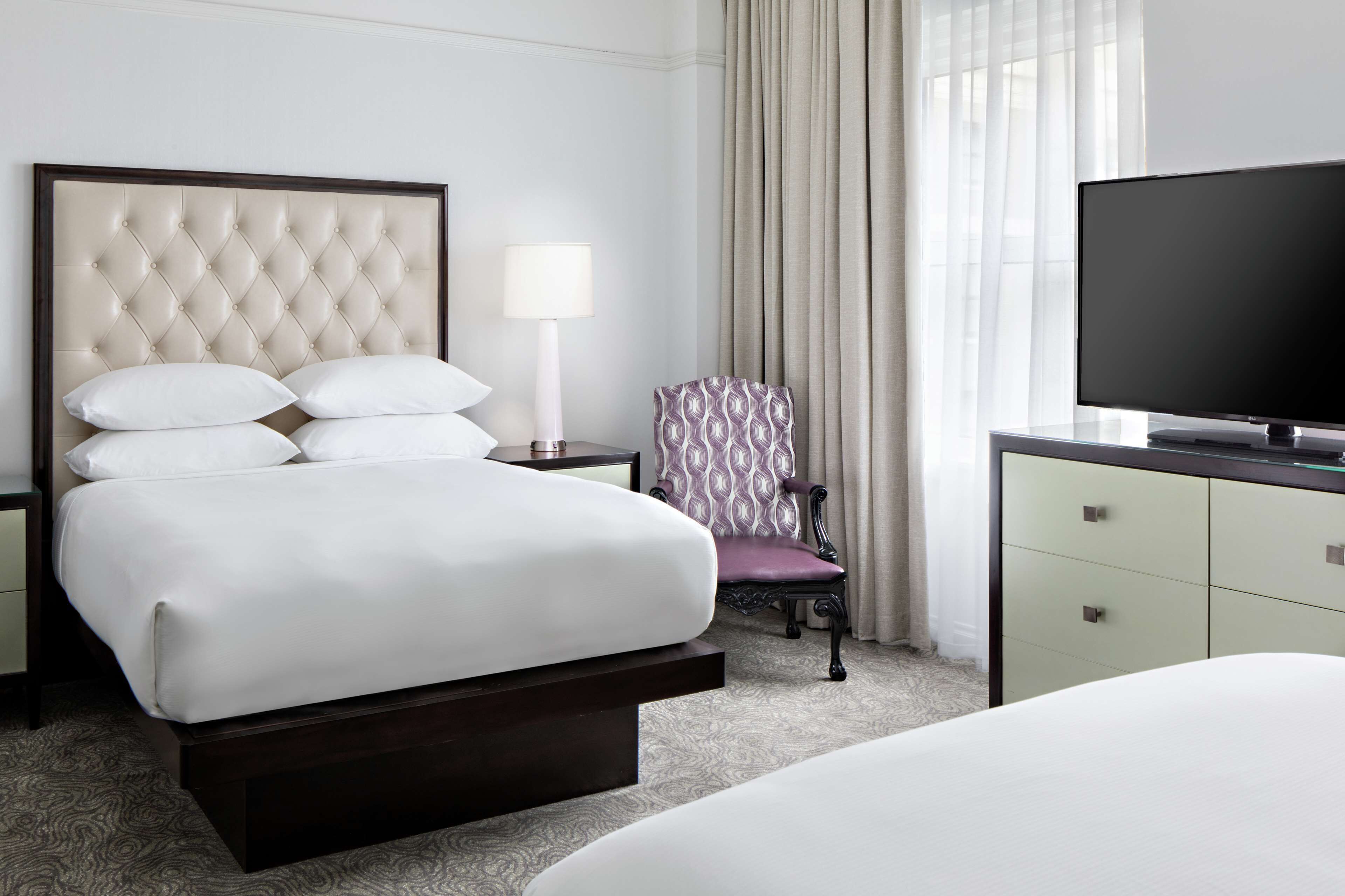 Ein Hotelzimmer mit einem großen Bett, einem Fernseher, einem Sessel und einem Schreibtisch.