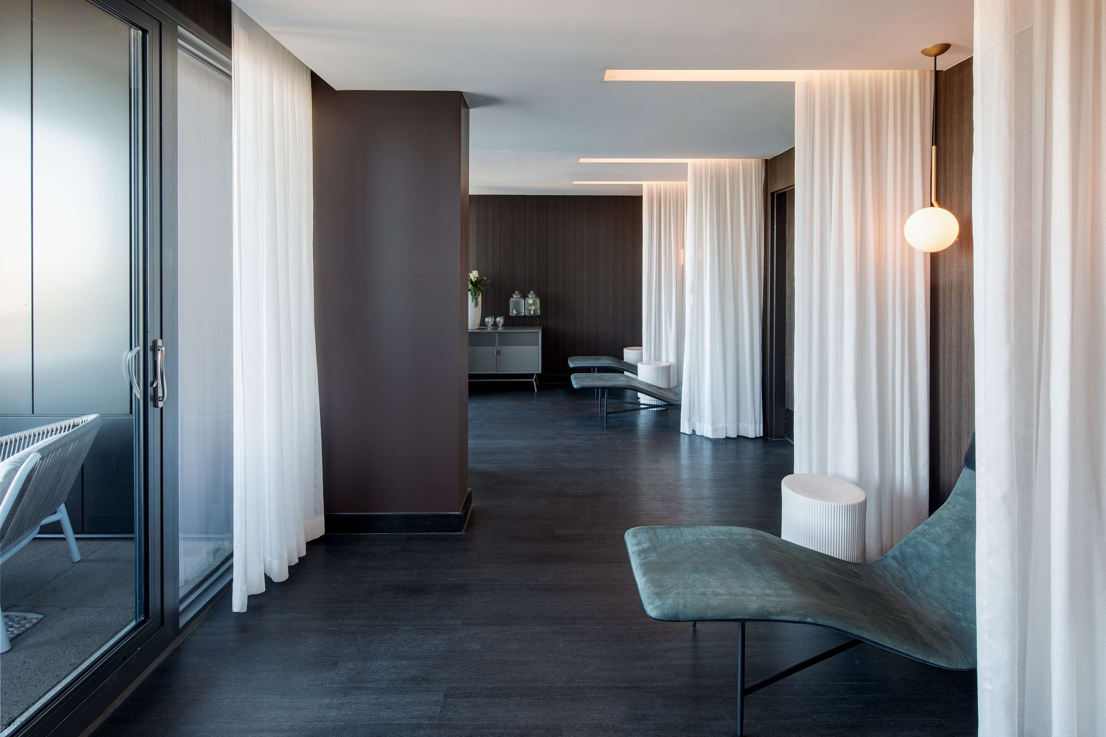 A modern hotel lobby with a glass partition, a seating area, and a reception desk.