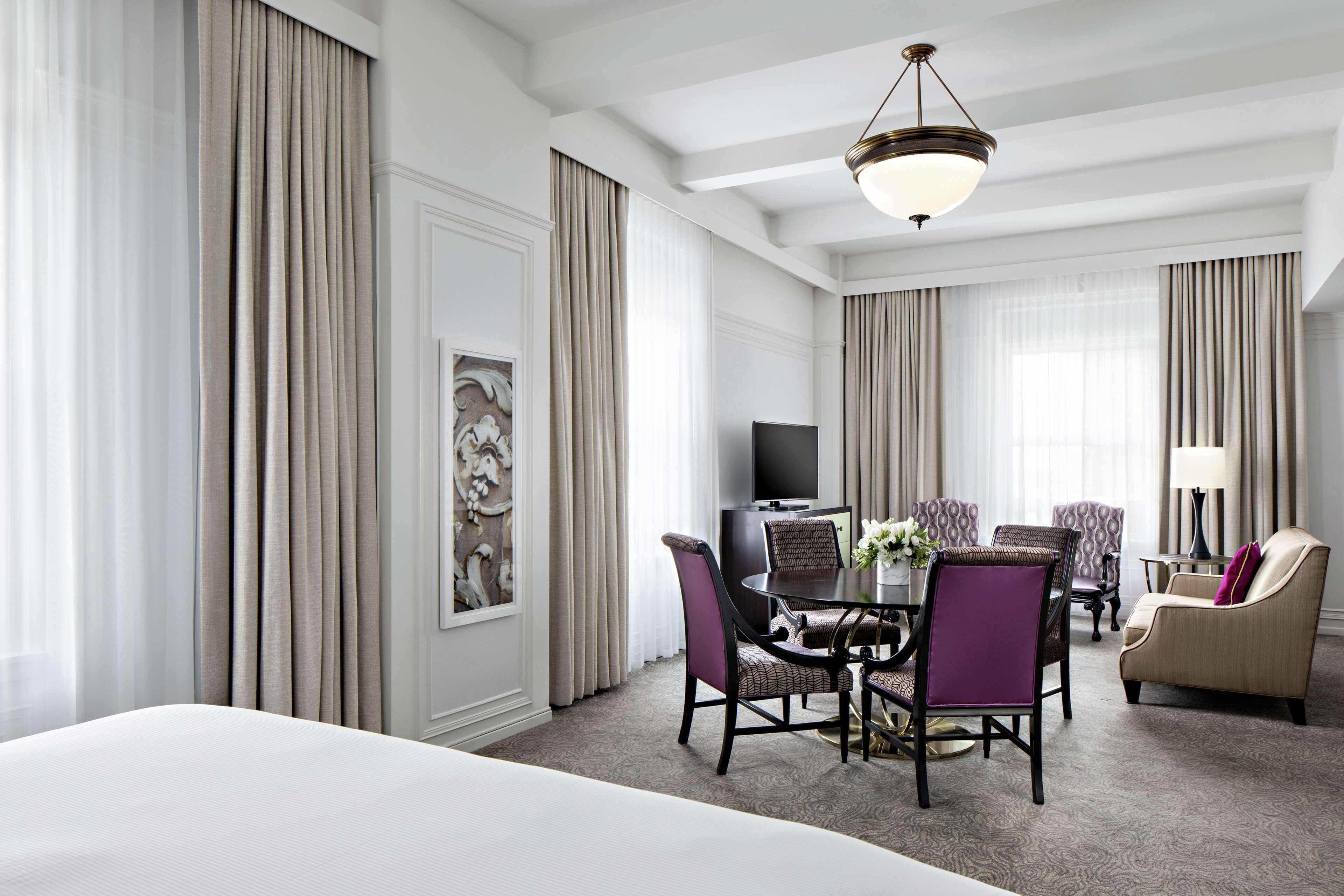 Una habitación de hotel con una cama grande, una mesa de comedor con sillas, un televisor y un sofá.