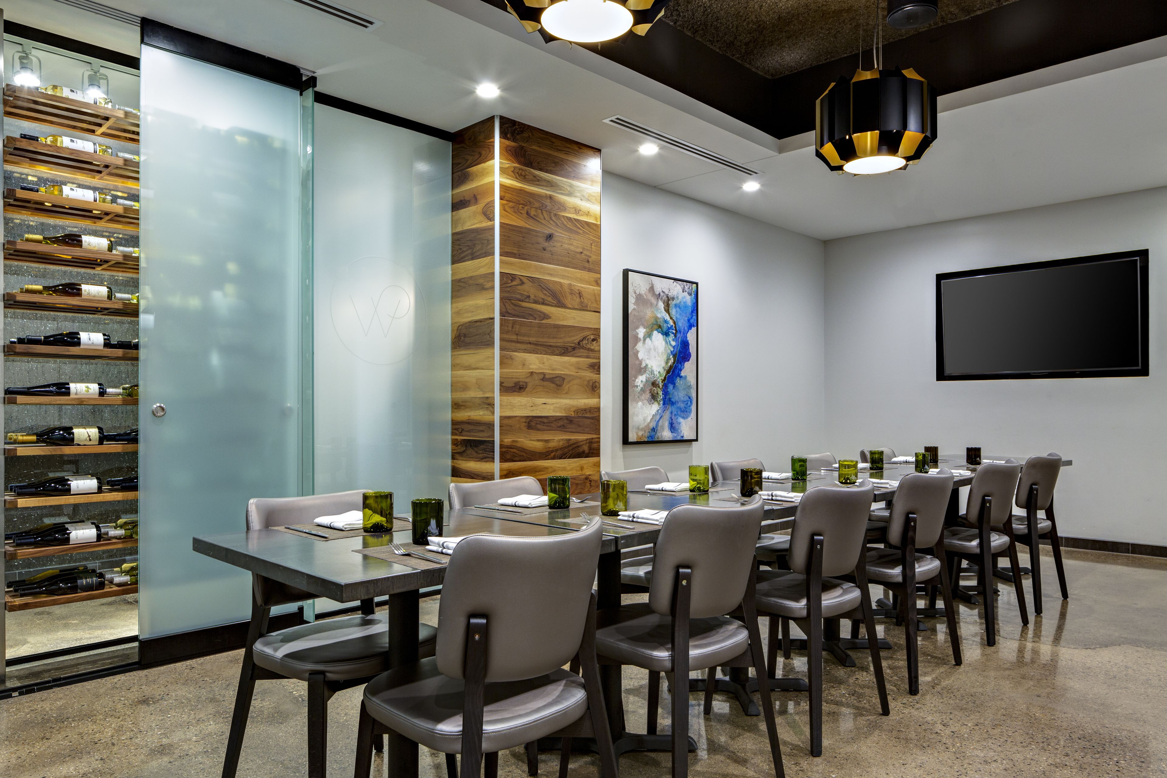 Un salón de conferencias con una larga mesa, sillas, una estantería para vinos y un cuadro grande en la pared.