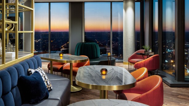 A modern lounge with a city view, featuring a sofa, round tables, and vibrant chairs. - Amway Grand Plaza, Curio Collection by Hilton (Grand Rapids)