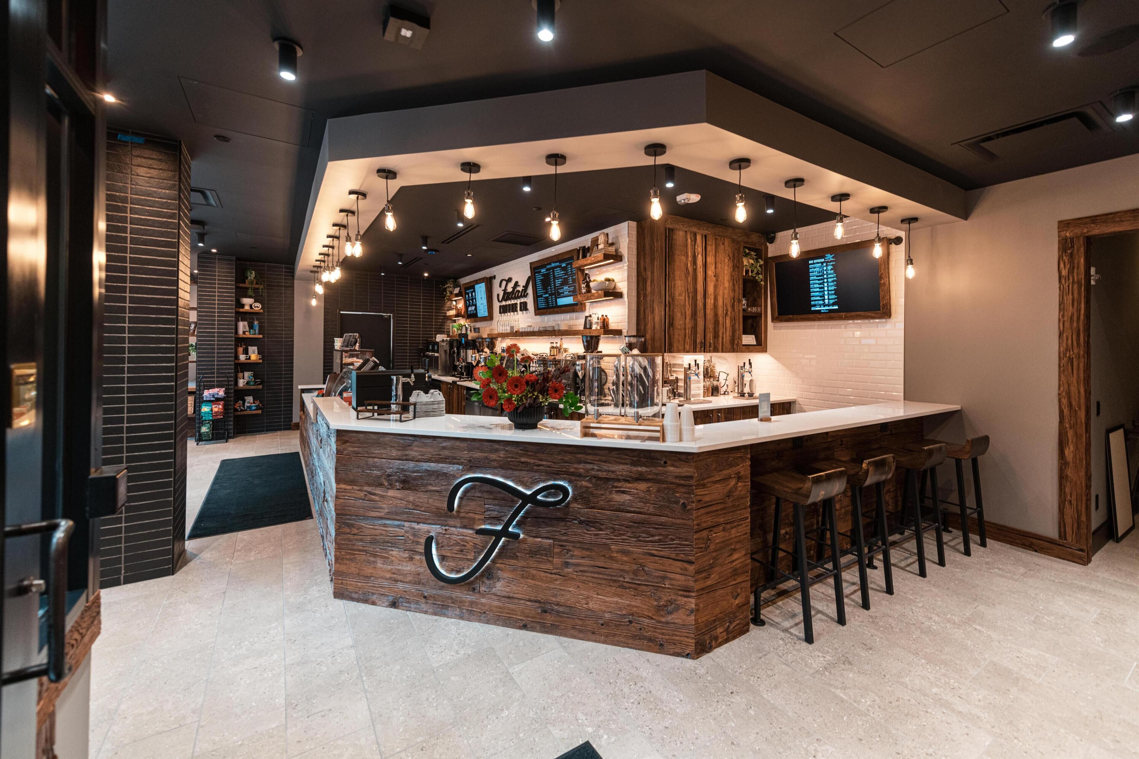 Un espace bar moderne avec un comptoir en bois, des tabourets de bar et des luminaires suspendus.