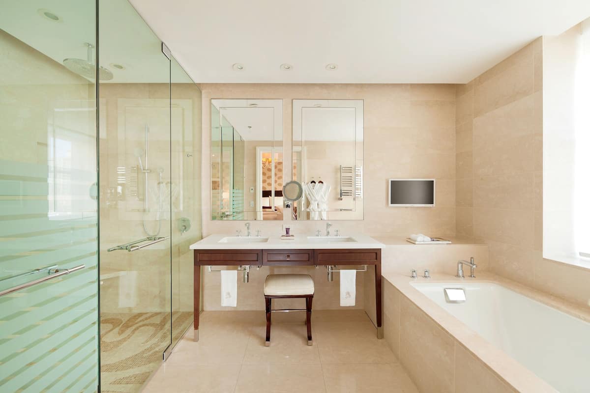 A modern bathroom with a glass shower enclosure, a double vanity with a large mirror, and a separate bathtub.