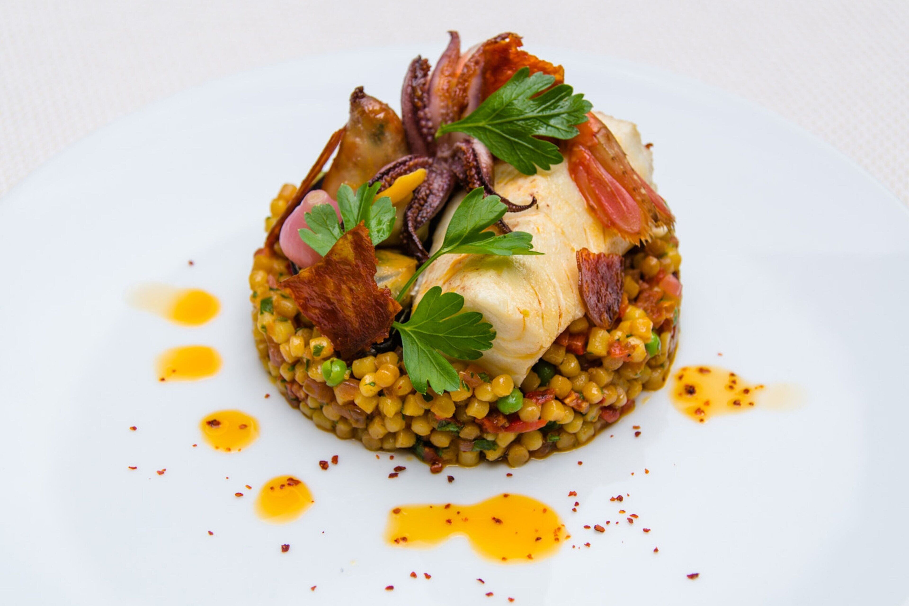 Un plat composé d'un morceau de poisson, de légumes verts et de lardons, le tout servi sur un lit de lentilles, dans une assiette blanche.