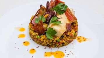 Un plat composé d'un morceau de poisson, de légumes verts et de lardons, le tout servi sur un lit de lentilles, dans une assiette blanche.