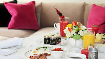 En frukostuppdukning med tallrikar fyllda med mat, en kaffekopp och en kanna med apelsinjuice på ett bord.