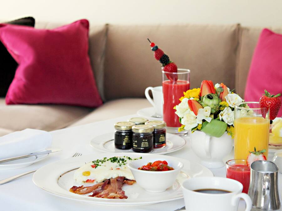 En frukostuppdukning med tallrikar fyllda med mat, en kaffekopp och en kanna med apelsinjuice på ett bord.