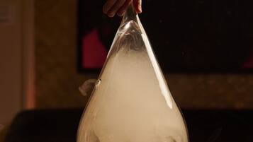 A hand holding a transparent glass dome over a drink on a coaster.