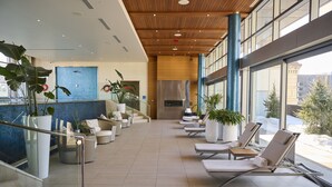 Un espace intérieur spacieux, aménagé avec des fauteuils confortables, de grandes plantes en pot et offrant une vue sur l’extérieur.