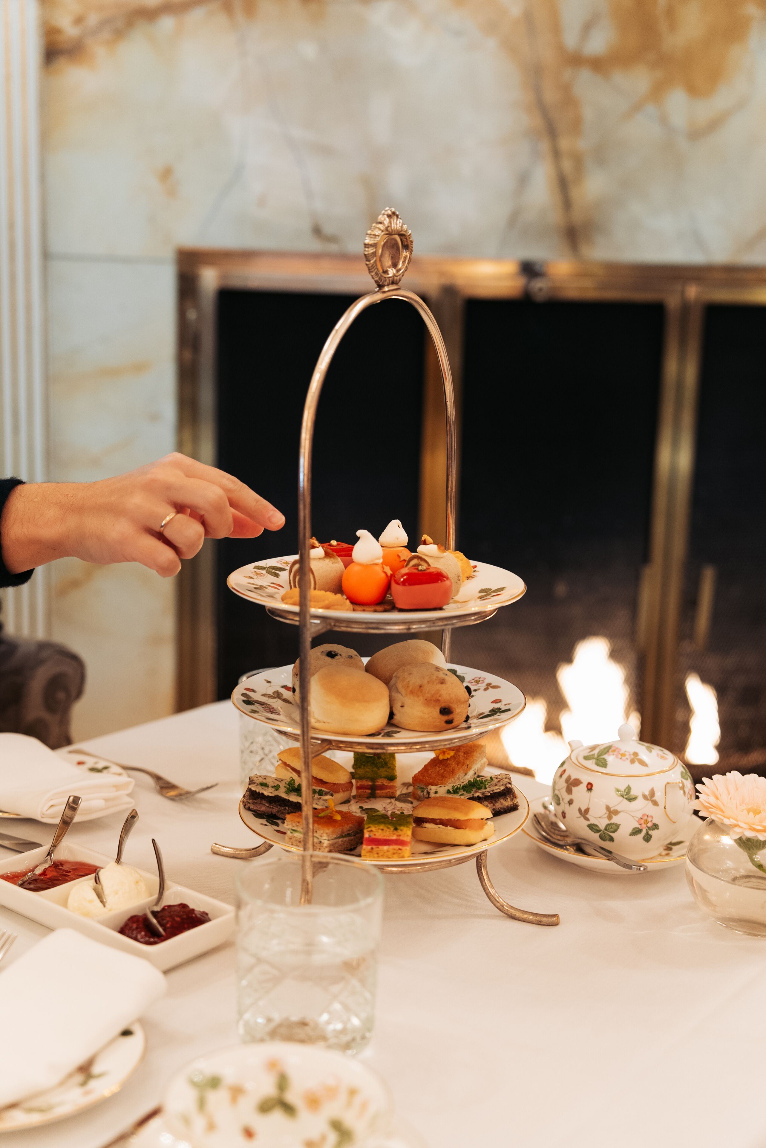 A tiered dessert stand with various pastries and a teapot on a table.