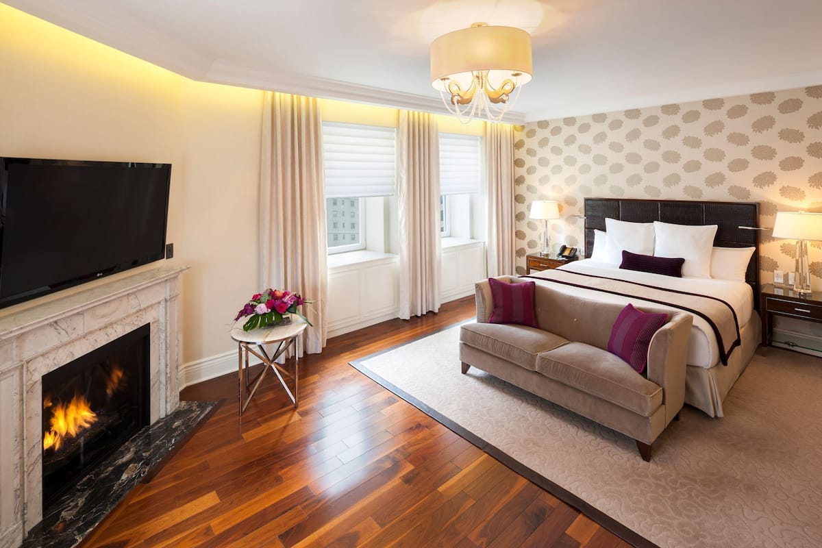 A hotel room with a fireplace, a television, a bed with a headboard, and a sofa.