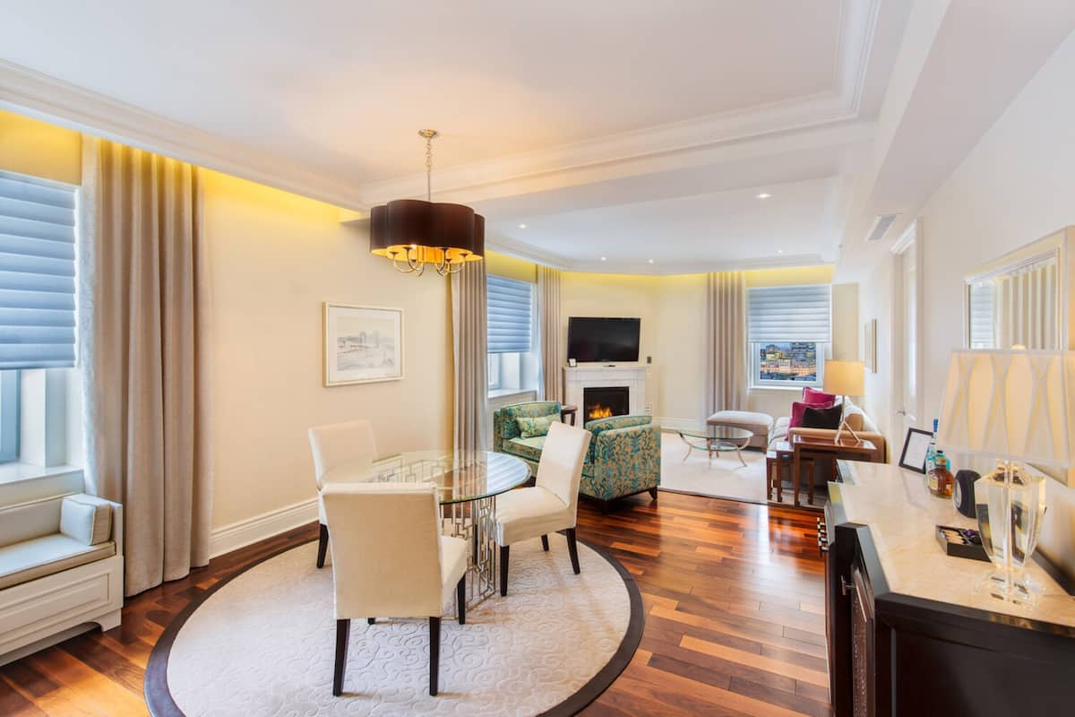 A modern hotel room with a round dining table, a sofa, a TV, and a fireplace.