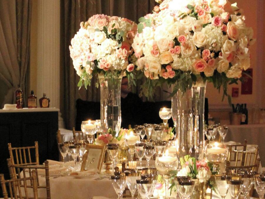 Una mesa dispuesta para un evento formal, con altos jarrones de flores, copas de vino y velas.