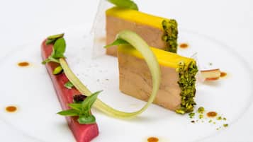 Un plato de postre con dos porciones de pastel, decorado con hojas verdes y adorno verde.