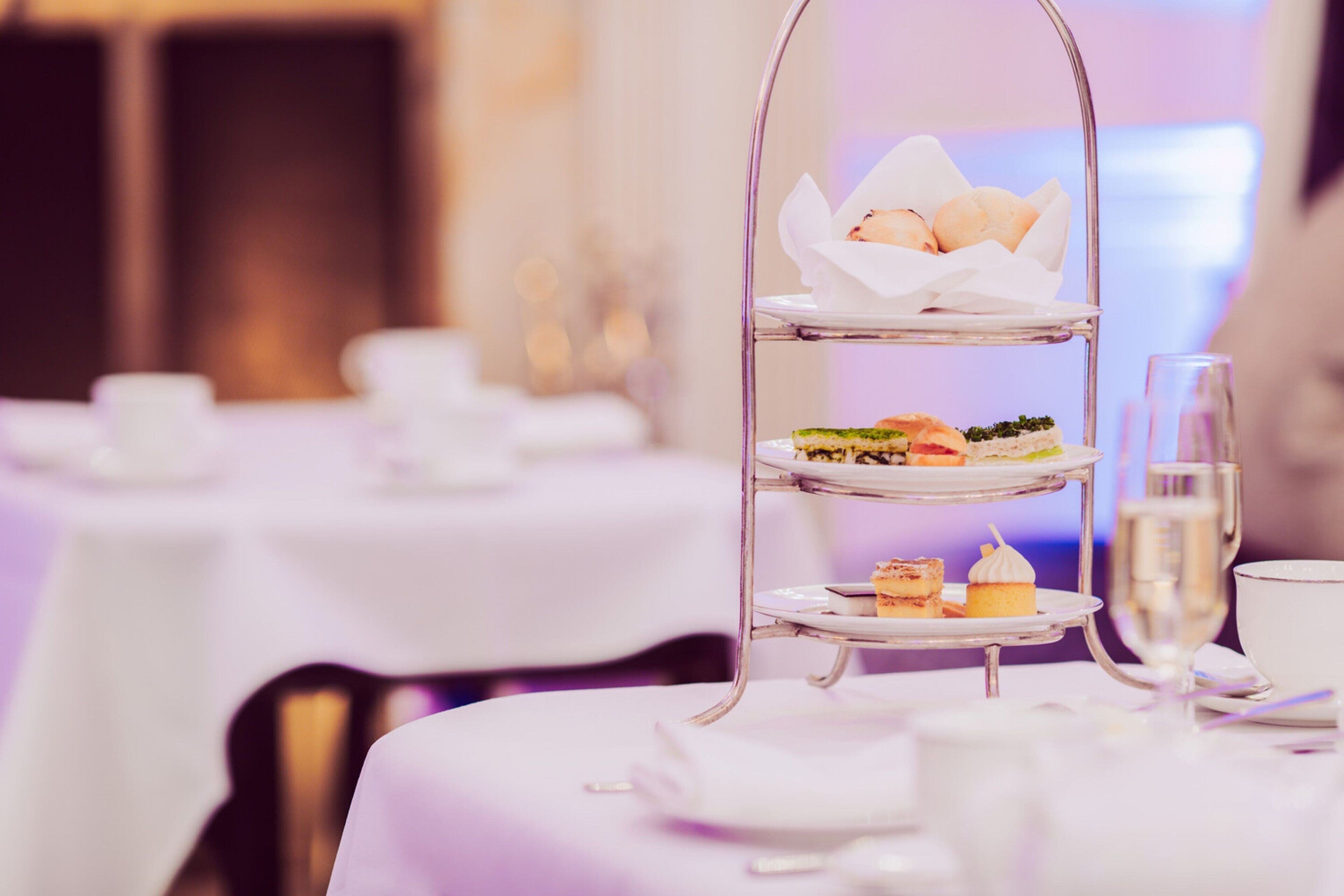 Un présentoir à trois niveaux, garni de diverses pâtisseries et de sandwichs, est placé sur une table dans un espace dédié à la restauration.