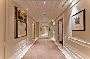 A hallway with a patterned carpet, framed artwork on the walls, and doors leading to rooms.