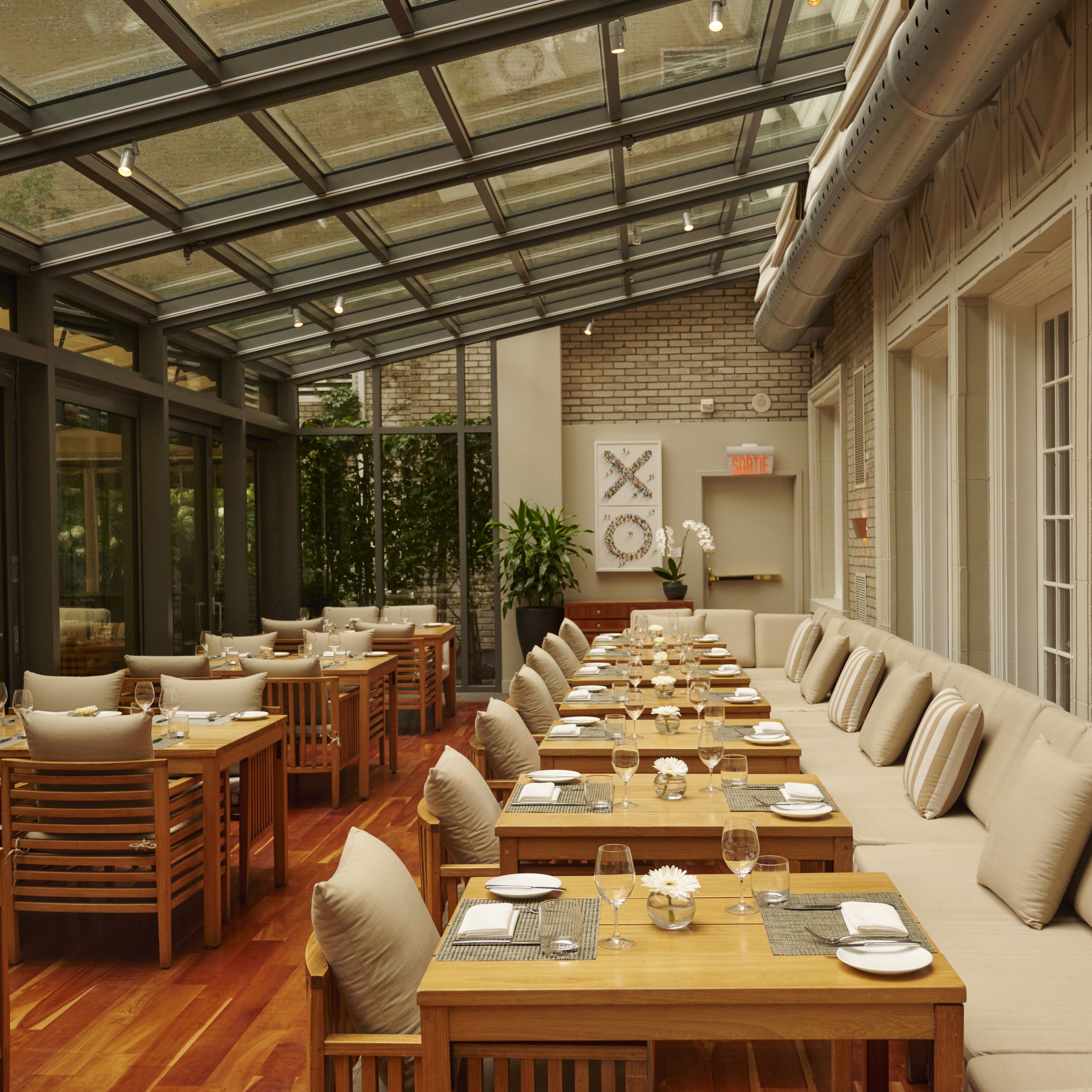 Un restaurante con una larga mesa de madera dispuesta para comer, un área de sofás y un techo de cristal.