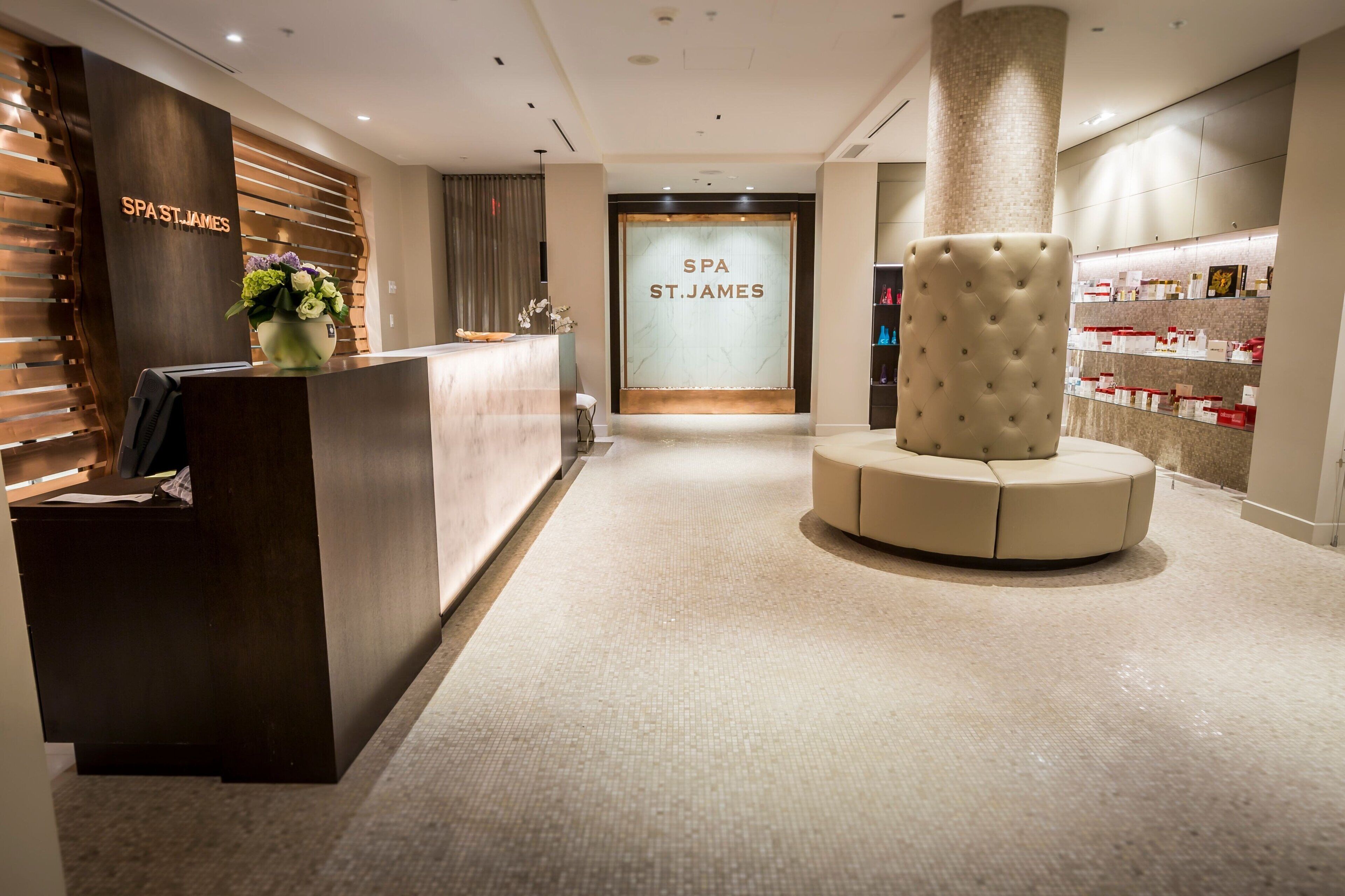 A reception area with a wooden reception desk, a large glass door labeled "SPA ST. JAMES", and a seating area with a tufted ottoman.