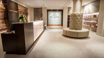 A reception area with a wooden reception desk, a large glass door labeled "SPA ST. JAMES", and a seating area with a tufted ottoman.