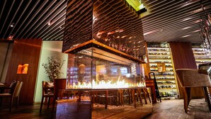 L’intérieur d’un restaurant, avec un foyer central, des meubles en bois et un présentoir à vin en arrière-plan.