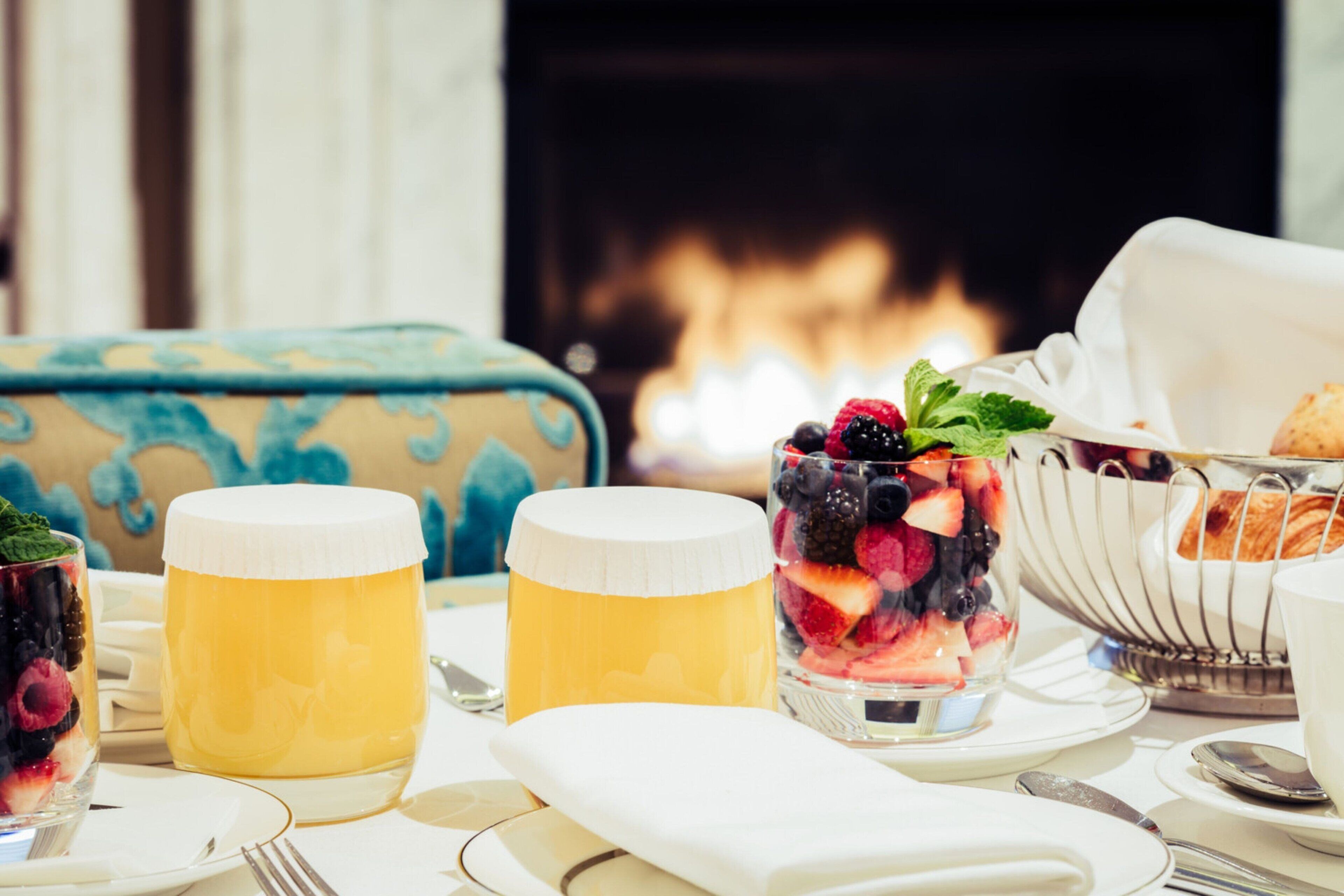 A breakfast setting with fruit bowls, honey jars, and a basket of croissants.