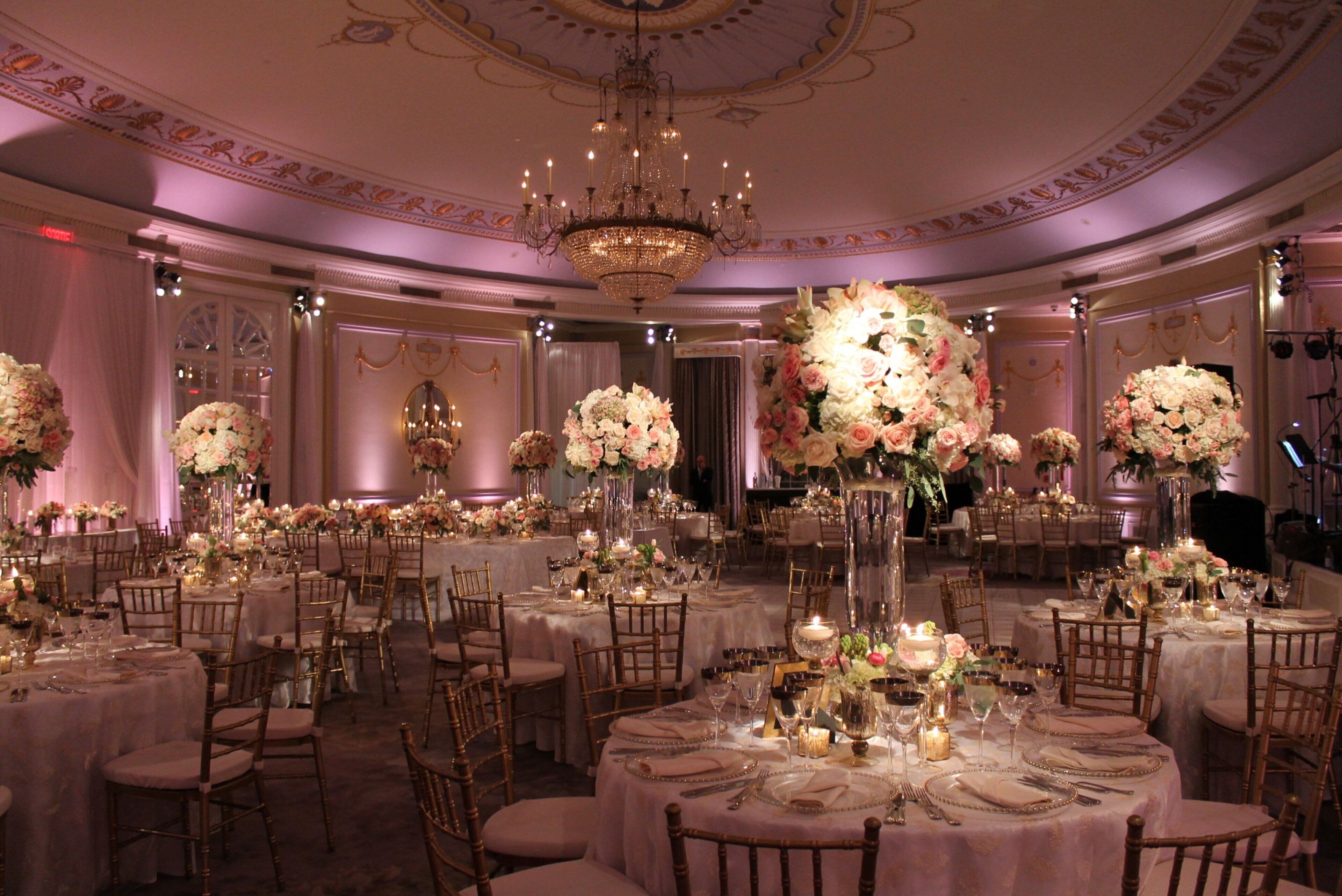 A banquet hall with round tables, chairs, and floral centerpieces.