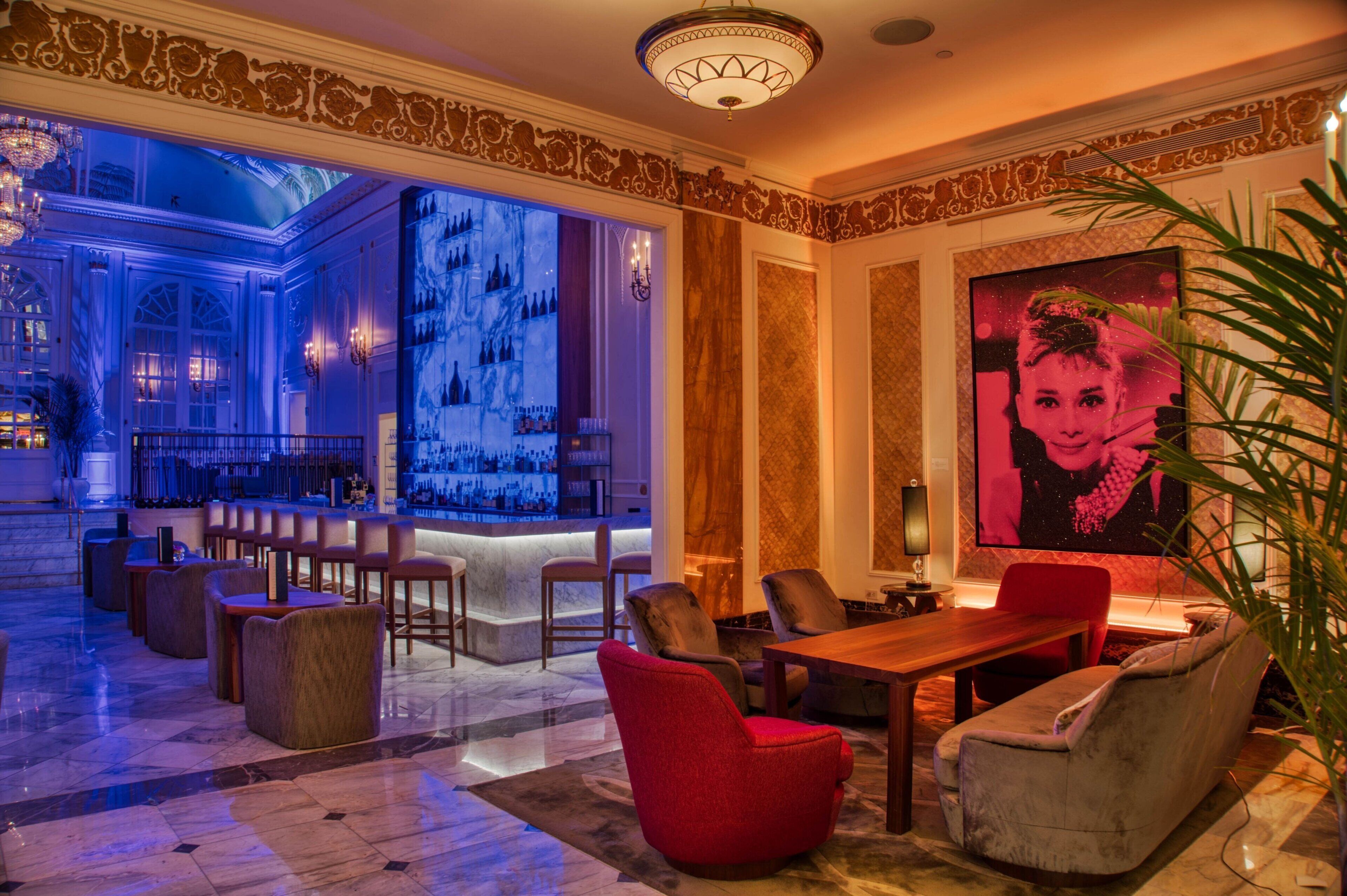 A lobby with a bar area, seating, and a large screen displaying a pink-toned image.