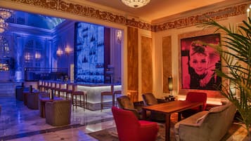 A lobby with a bar area, seating, and a large screen displaying a pink-toned image.