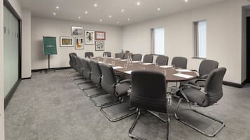 A conference room with a large oval table, black chairs, and a projector screen.