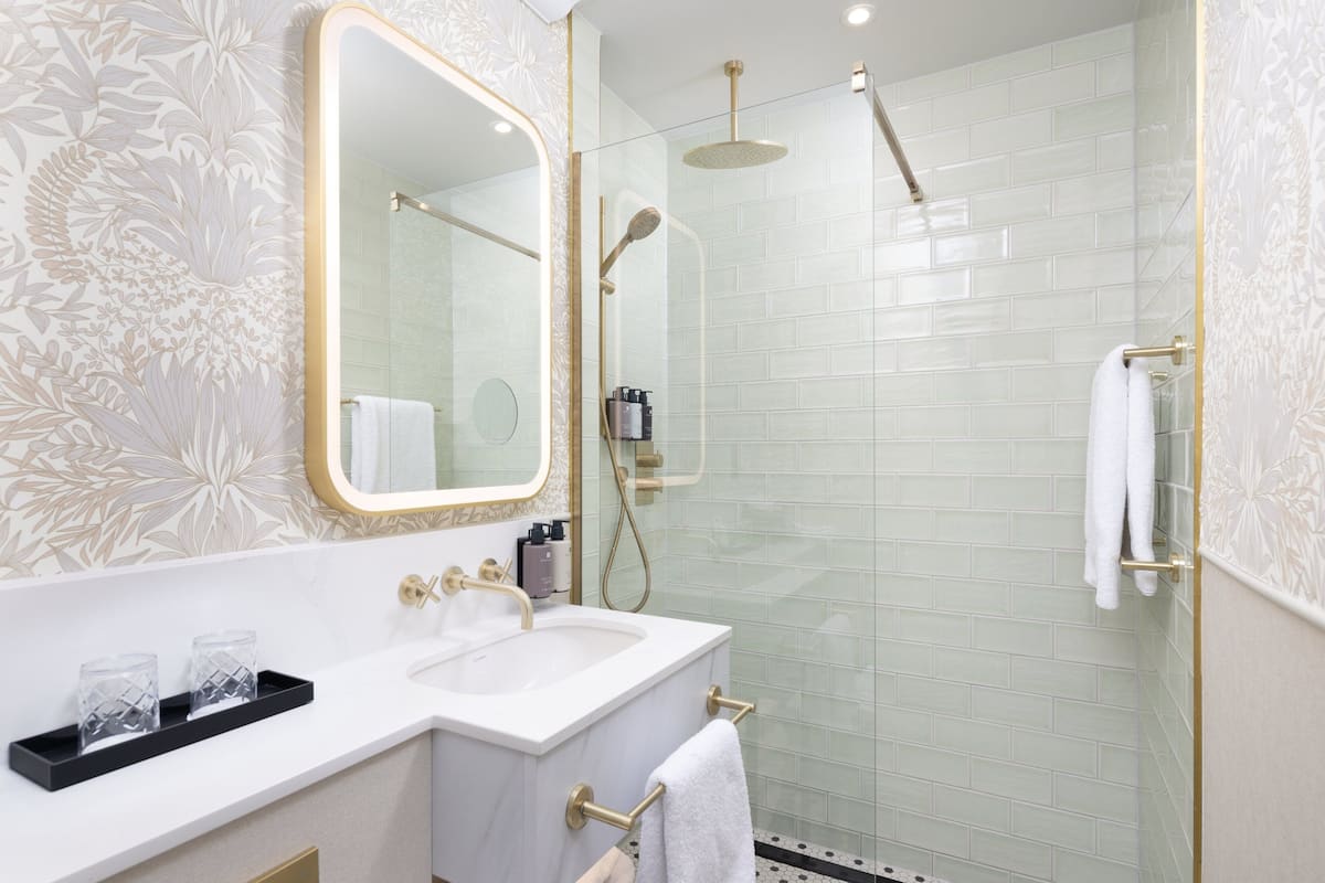 A modern bathroom with a glass-enclosed shower, a white sink with gold fixtures, and a large mirror.