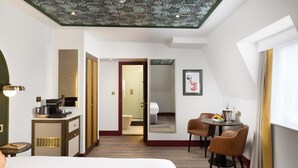 Ein Hotelzimmer mit einem Bett, einem Schreibtisch mit Stuhl, einem Spiegel und einer Essecke mit Tisch und Stühlen.