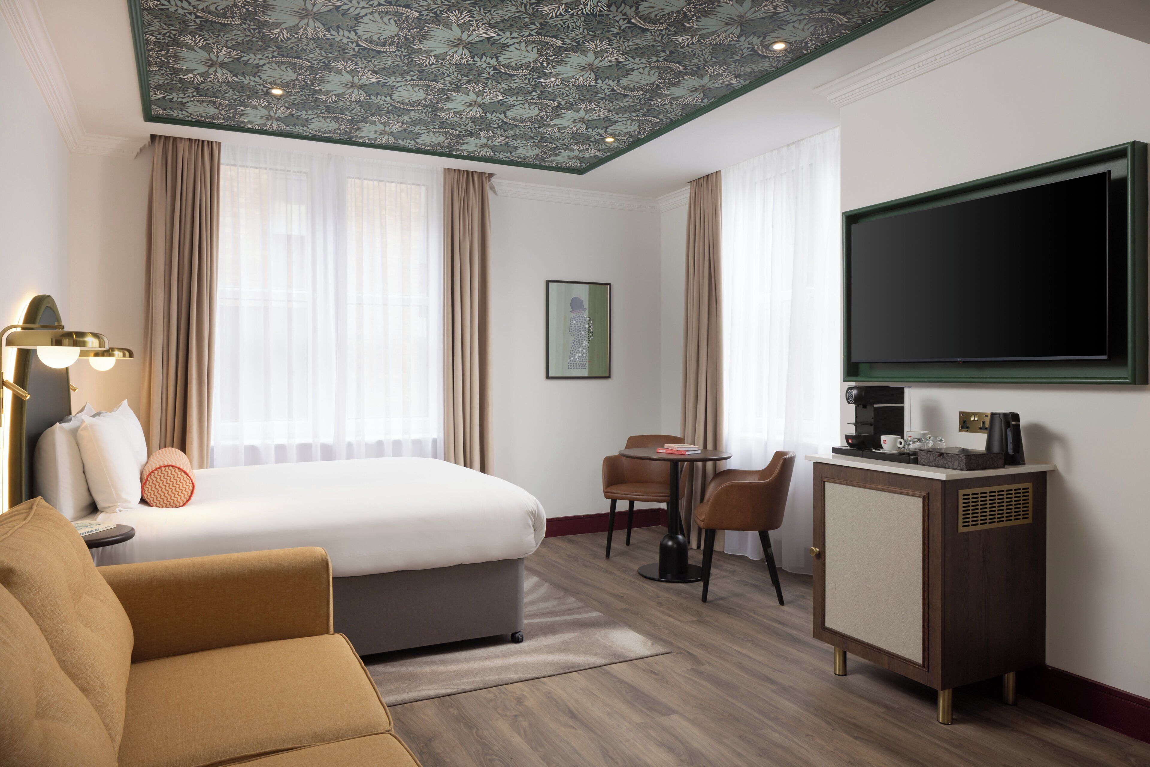 A hotel room with a bed, a sofa, a desk with a chair, a TV, and a coffee machine.
