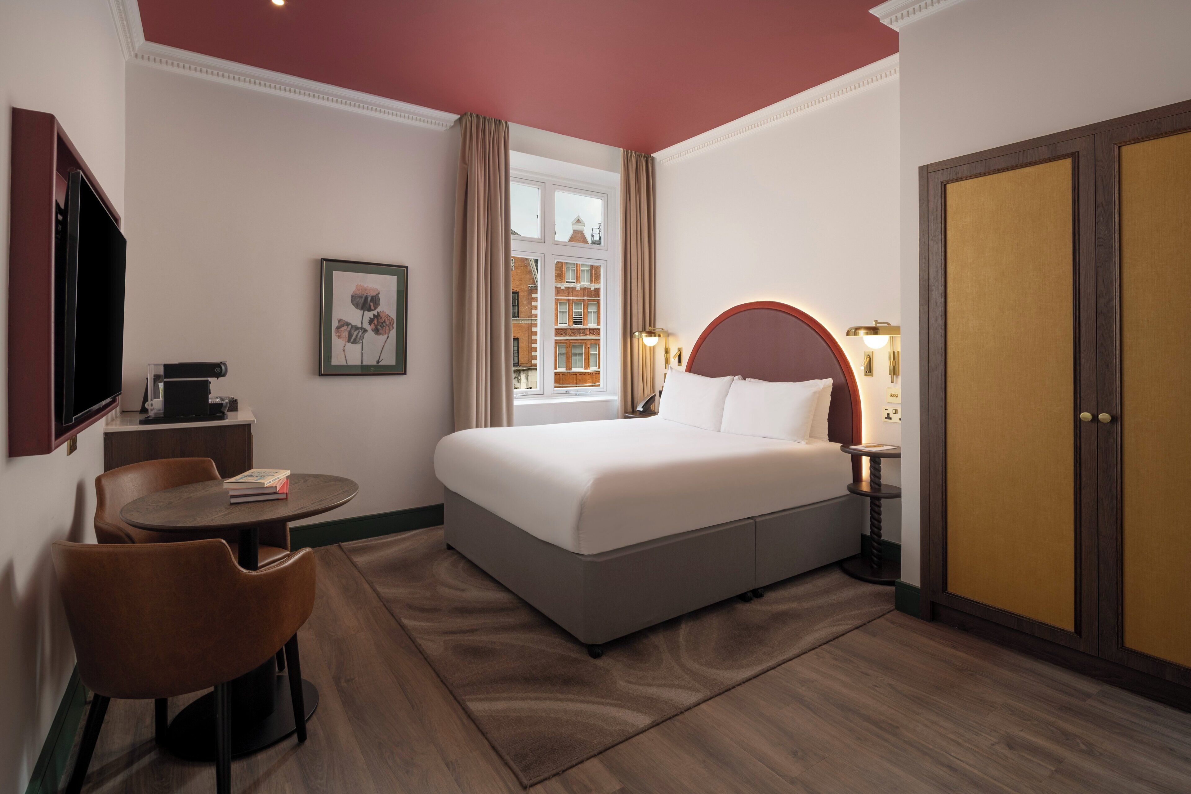 A hotel room with a large bed, a desk with a chair, a television, and a window with curtains.
