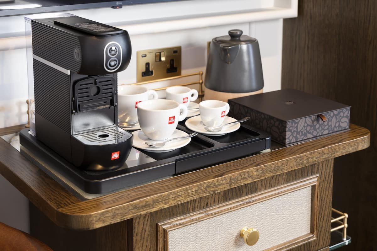 A coffee station with a coffee maker, cups, and a kettle on a wooden counter.