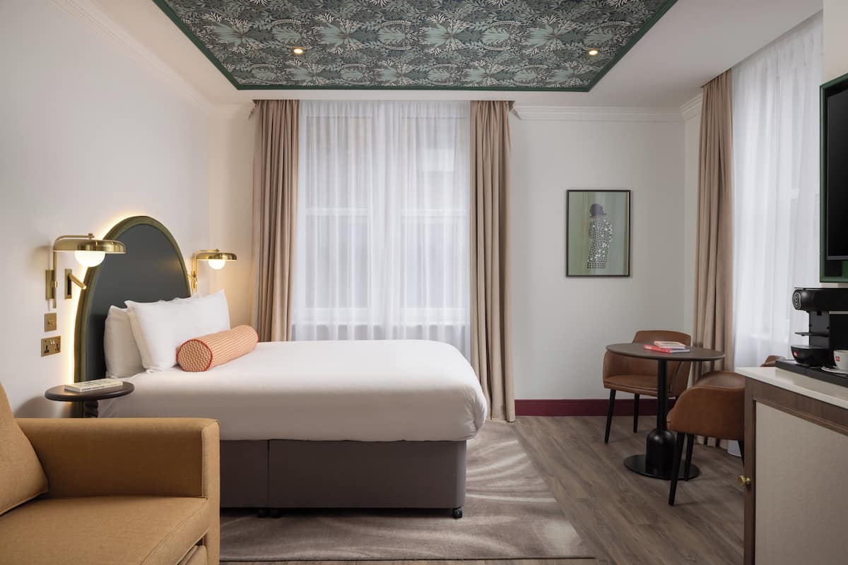 A hotel room with a bed, a desk, a chair, and a coffee machine.