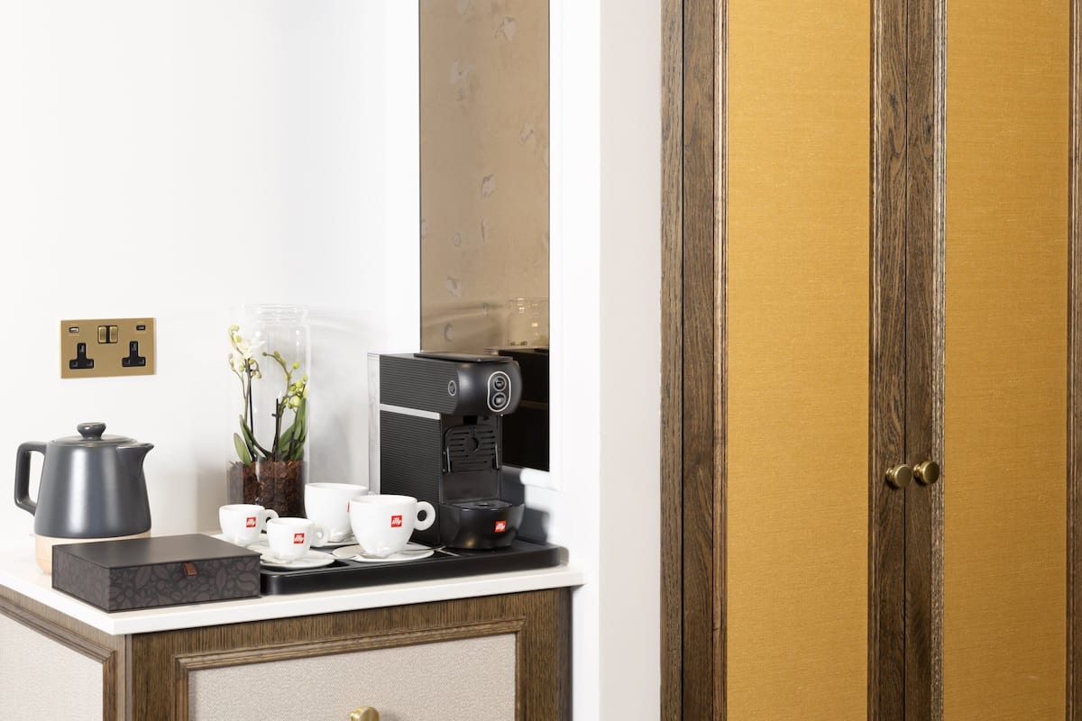 A kitchenette with a coffee maker, cups, a kettle, and a vase of flowers.