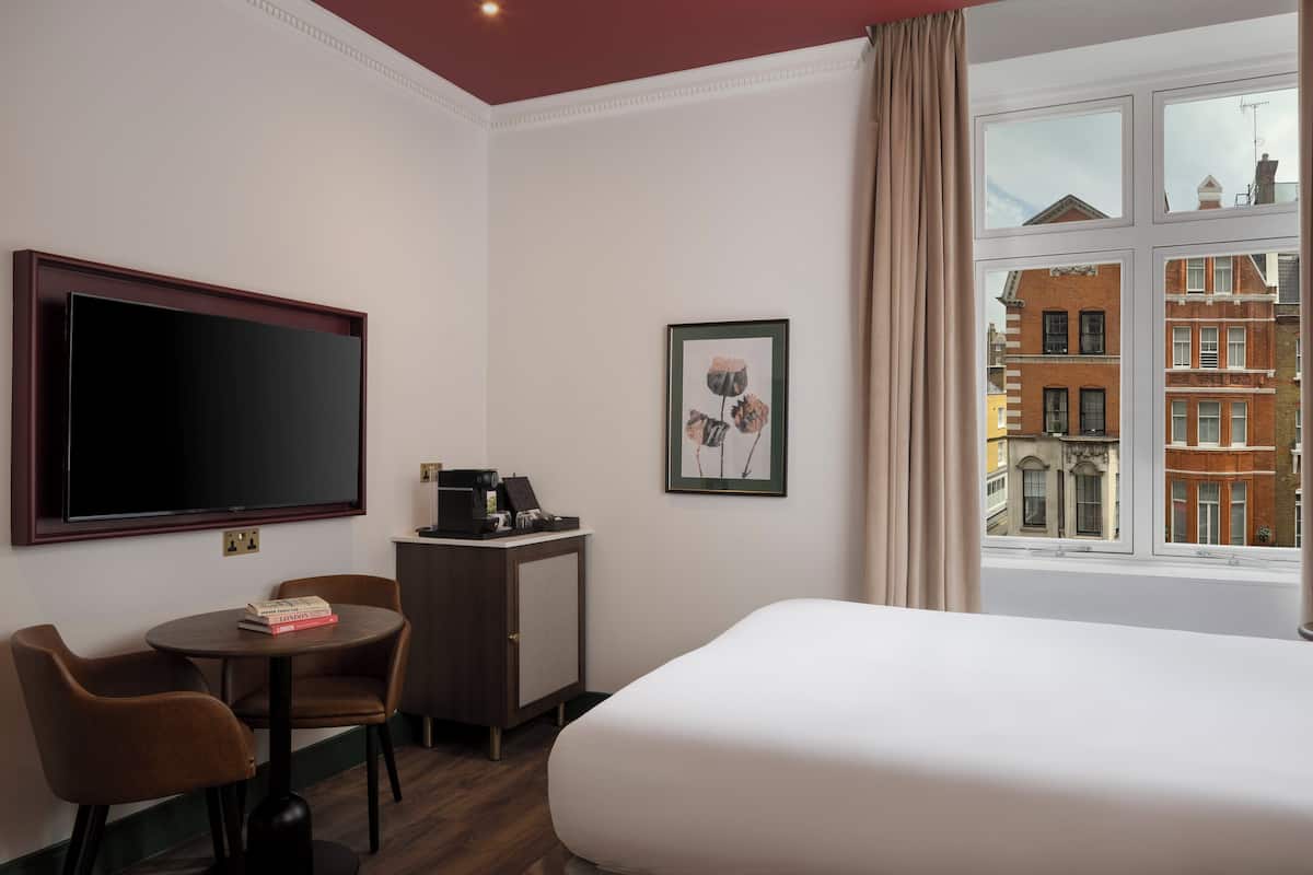 A hotel room with a bed, a desk with a coffee machine, a TV, and a window with a city view.